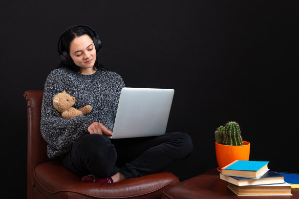 一名十几岁的女性，带着笔记本电脑、耳机和泰迪熊，在家远程在线学习图片下载