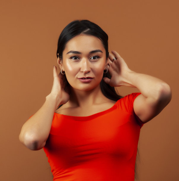 年轻漂亮的亚洲女人开朗的微笑摆姿势在温暖的棕色背景，生活方式的人的概念图片下载