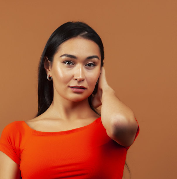 年轻漂亮的亚洲女人开朗的微笑摆姿势在温暖的棕色背景，生活方式的人的概念图片下载