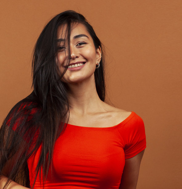 年轻漂亮的亚洲女人开朗的微笑摆姿势在温暖的棕色背景，生活方式的人的概念图片下载