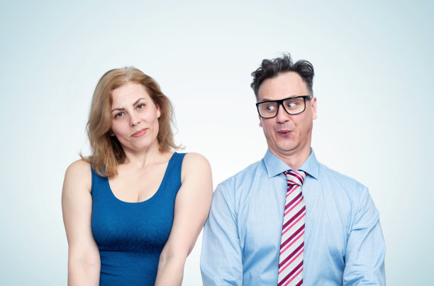 在浅蓝色的背景上，一个戴着眼镜、打着领带的滑稽男子斜视着旁边一个穿着紧身连衣裙的年轻女子的半身像图片下载