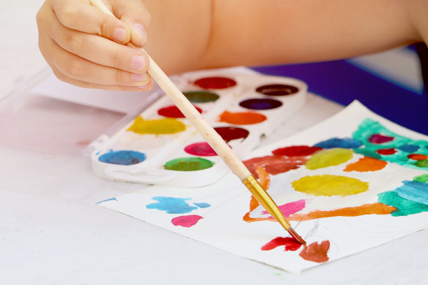 孩子拿着画笔，还有颜料和绘画工具。一个孩子的手的特写照片。回到学校的概念。副本的空间。图片下载