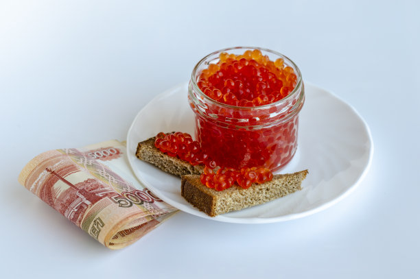 一个装着红色鱼子酱的玻璃罐，白色盘子上放着一片片黑面包，上面印着俄罗斯货币图片下载