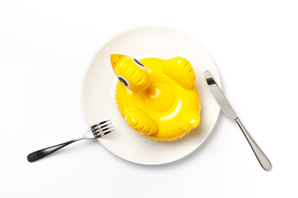 白色盘子上的充气迷你黄鸡或小鸭，白色背景上的餐叉刀。创意食品理念，烟草鸡。潮流充气游泳儿童玩具。布局设计图片下载