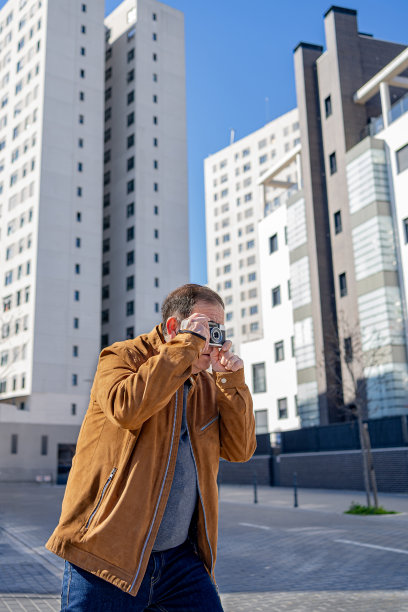 一位老人在城市里用旧胶卷相机拍照。图片下载
