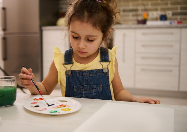小白种人女孩坐在木桌旁，用画笔在调色板上调出水彩画或水粉画，享受绘画图片下载