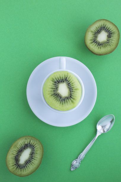 白色茶杯，绿色的背景上放着新鲜的切成两半的猕猴桃。前视图。副本的空间。图片下载