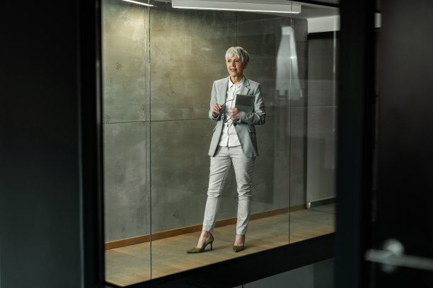 快乐的高级女商人站在办公楼的走廊里。图片下载