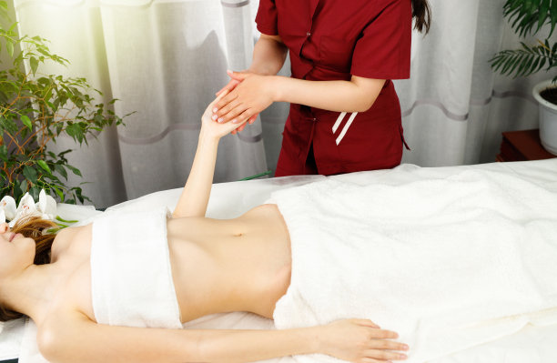 剪裁照片的专业按摩师，以一个年轻的女性客户手按摩在水疗沙龙当她躺在按摩台。图片下载