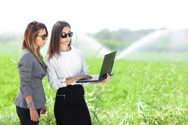 商业女性在有农业灌溉系统的田地里用笔记本电脑。图片下载