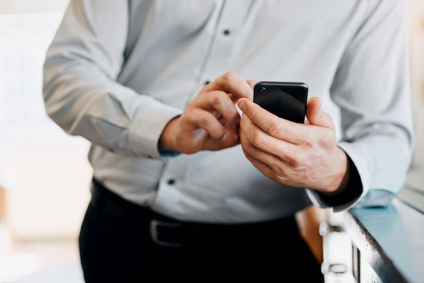 剪裁的照片一个不知名的商人独自站在办公室里用他的手机图片下载