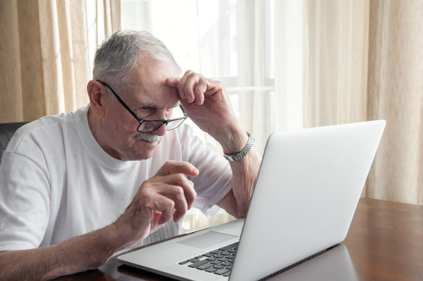 一位老人坐在家里的笔记本电脑前思考着。一位戴着眼镜、头发花白的老人坐在家里的笔记本电脑前工作。老年人之间沟通的概念图片下载