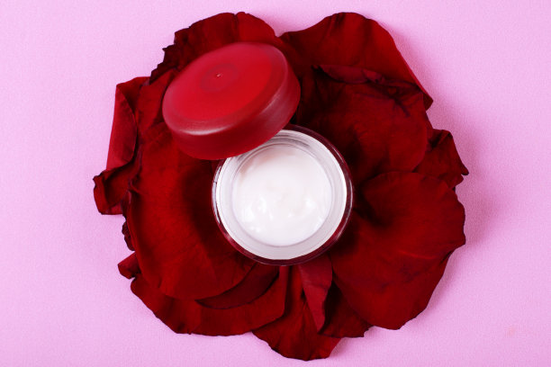保湿霜罐在红色玫瑰花瓣上在粉色上图片下载