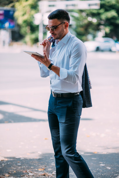 一个年轻的经纪人在高峰时间站在繁忙的街道旁看着他的平板电脑图片下载