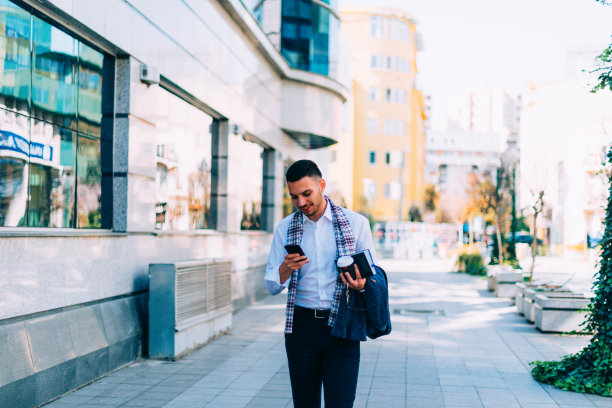一个穿西装的男人站在城市广场上，环顾四周，用手机打电话。图片下载