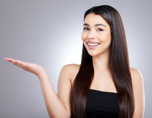 工作室的肖像，一个有魅力的年轻女子指着在灰色背景下的copyspace图片下载