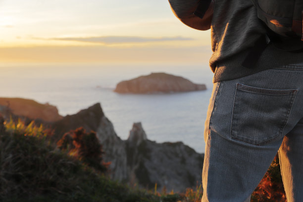 近距离拍摄的侧面和大腿的一个无法辨认的人享受日落在海上，利用选择性聚焦。旅行和健康的概念。图片下载