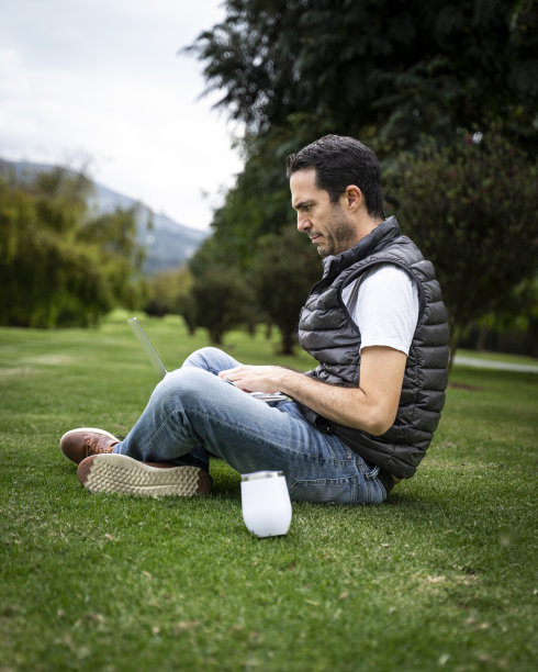 一个男人坐在草地上用笔记本电脑图片下载