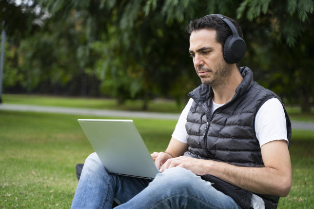 白人男子在户外用耳机和笔记本电脑工作图片下载