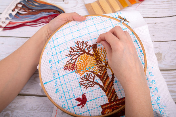 画布上的女孩用毛线和针线绣出了彩色的鸟和带十字记号的树图片下载
