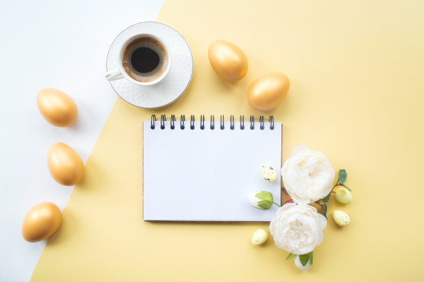 金色的复活节彩蛋，咖啡杯，精致的花和笔记本与地方的文本在黄色的背景上。时髦的公寓。最小的概念。图片下载