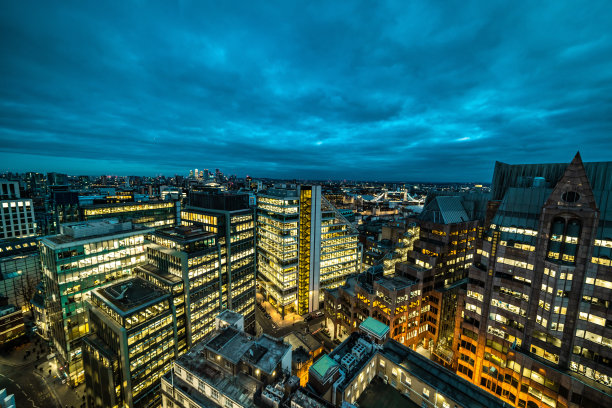 现代玻璃建筑在夜晚高高耸立在布鲁塞尔的天际线上，办公室灯火通明图片下载