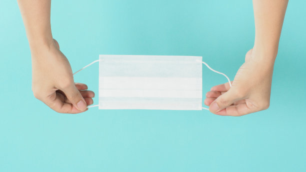 手拿白色面膜，薄荷或蒂芙尼蓝色背景。图片下载