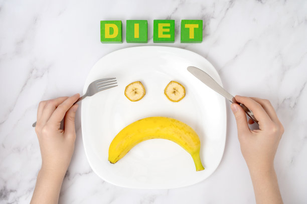 拒绝饮食。女性的手拿着叉子和餐刀，放在放着香蕉的盘子上。图片下载