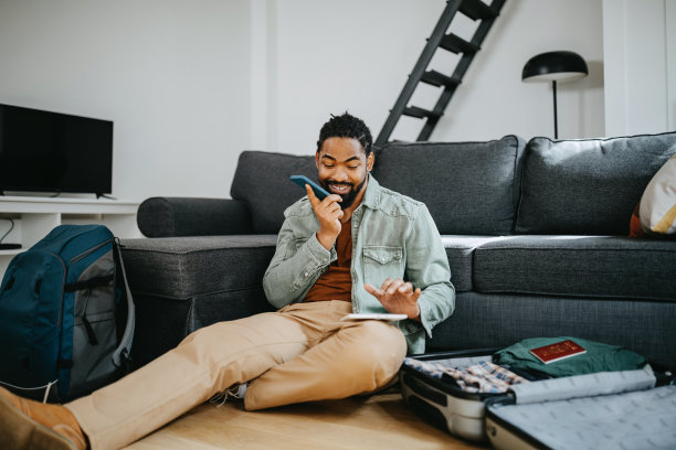 为旅行做准备。黑人在打电话，把衣服装进箱子里图片下载