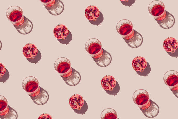 创意图案由一半石榴和玻璃与果汁或红酒在柔和的米色背景。夏日水果和清爽的概念。最小的风格。阳光公寓。俯视图图片下载