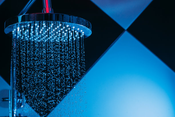 在淋浴时，蓝色的灯光下，水从喷壶里滴下来。水滴特写。流动的水。浴室里有一个大的圆形喷壶。图片下载
