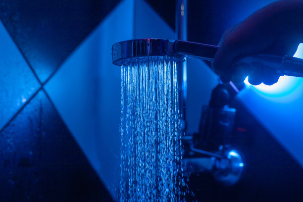 一个女孩拿着一个洒水罐在一个有蓝色背光的淋浴房。从喷壶里滴下来的水。图片下载