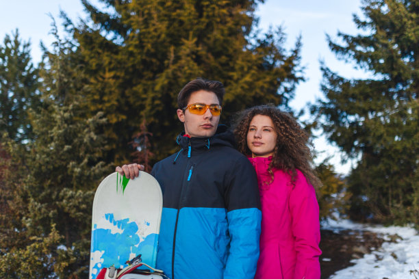 一对年轻的异性恋情侣在雪山顶上举着滑雪板摆姿势图片下载