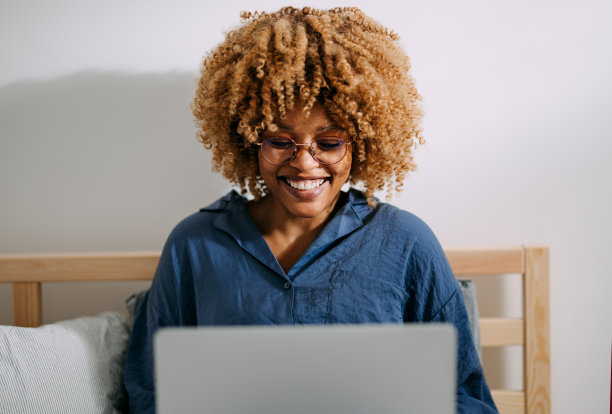快乐的女商人在床上使用笔记本电脑图片下载