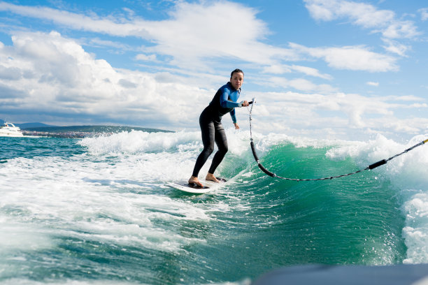 Watersport概念。年轻的女运动员学习水上冲浪和完善技巧。在阳光明媚的日子里，穿着潜水服的女性用拖绳在船后乘风破浪。图片下载