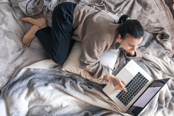 一个女人躺在床上用笔记本电脑工作，俯视图。图片下载