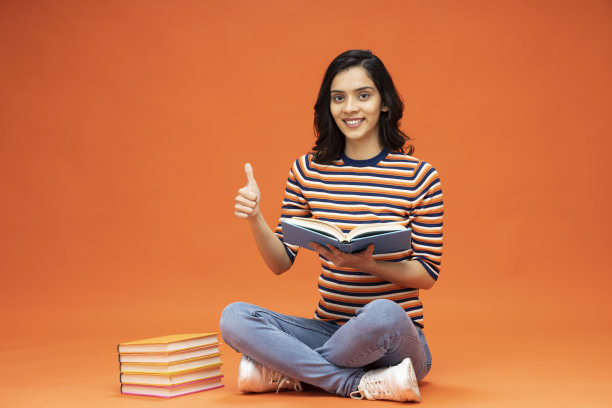 年轻女子坐在地板上，橙色背景的书，库存照片图片下载