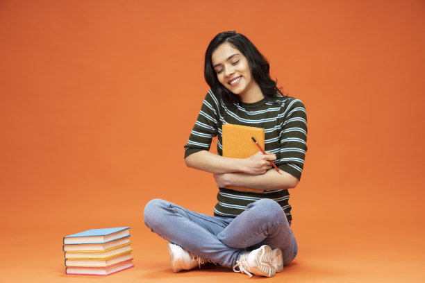 年轻女子坐在地板上，橙色背景的书，库存照片图片下载