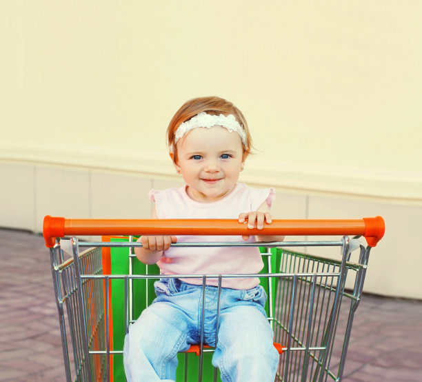 快乐的宝宝拿着购物袋坐在城市的手推车里图片下载