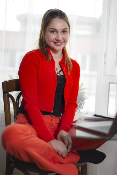 一个穿着红色开襟羊毛衫和红色裤子的小女孩在她学习的书桌前。图片下载