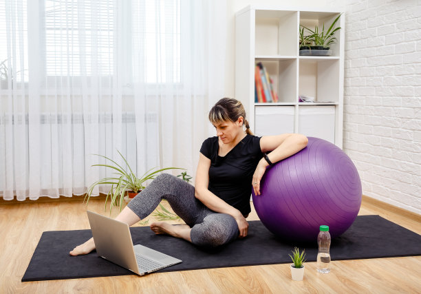 年轻运动女性坐在瑜伽垫上，隔离期间活动。图片下载