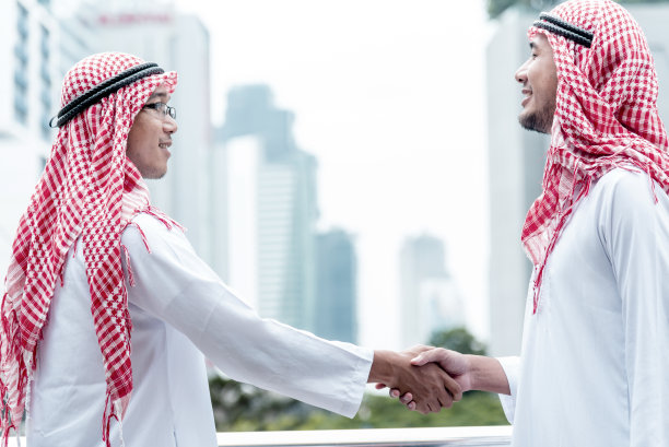 穿着穆斯林服装的阿拉伯商人，在阿联酋现代城市背景下握手。穆斯林团队合作的商业伙伴通过合作握手，多元种族阿拉伯人信任承诺图片下载