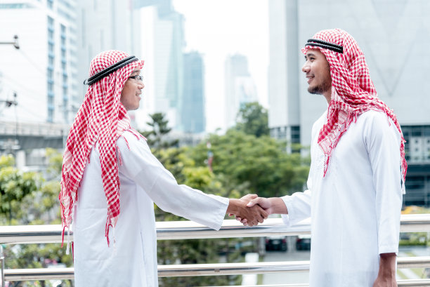 穿着穆斯林服装的阿拉伯商人，在阿联酋现代城市背景下握手。穆斯林团队合作的商业伙伴通过合作握手，多元种族阿拉伯人信任承诺图片下载