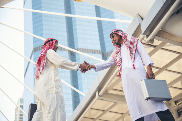 穿着穆斯林服装的阿拉伯商人，在阿联酋现代城市背景下握手。穆斯林团队合作的商业伙伴通过合作握手，多元种族阿拉伯人信任承诺图片下载