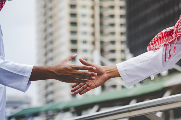 穿着穆斯林服装的阿拉伯商人握手合作。穆斯林男士团队与商业伙伴握手，建立商业伙伴关系。阿联酋多元种族人士信任承诺图片下载