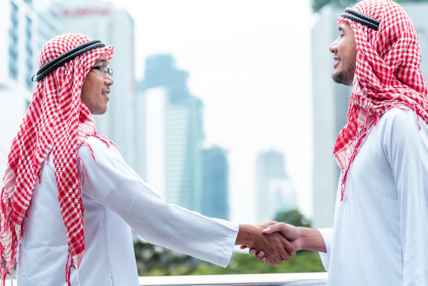 穿着穆斯林服装的阿拉伯商人，在阿联酋现代城市背景下握手。穆斯林团队合作的商业伙伴通过合作握手，多元种族阿拉伯人信任承诺图片下载