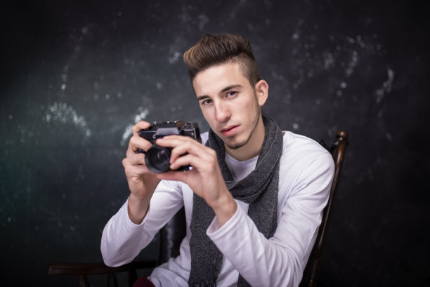 摄影棚里一个英俊的年轻人拿着相机的肖像。图片下载