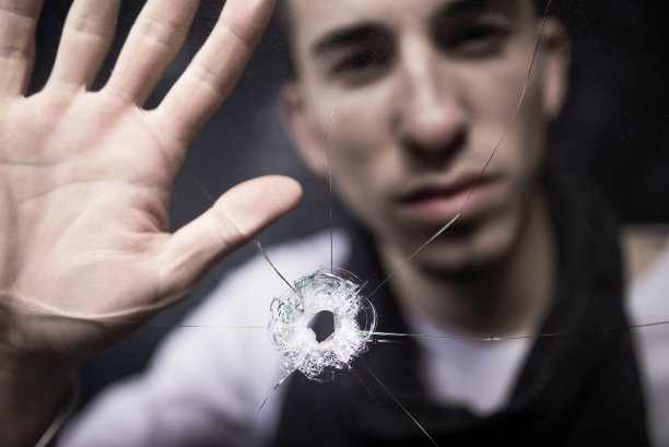 一个年轻人正把手放在被撞裂的玻璃上。图片下载