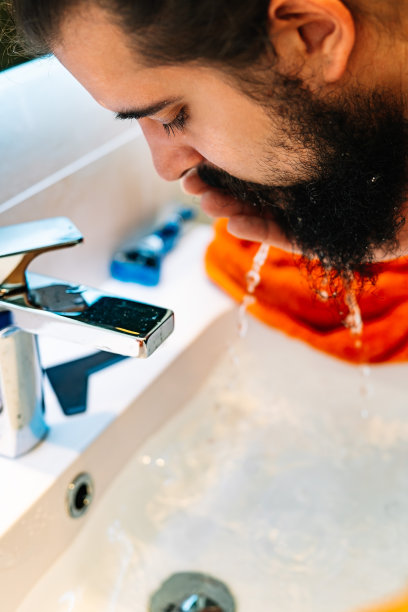 一个留着浓密胡子的年轻男子的特写，在浴室的水槽里洗脸图片下载