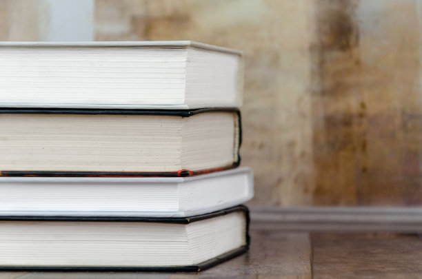 堆叠在桌子上的书靠在有纹理的混凝土墙上。理念教育，阅读，桌面。图片下载